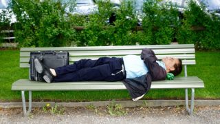 公園のベンチに腕を組んで不機嫌そうに寝転がる男性